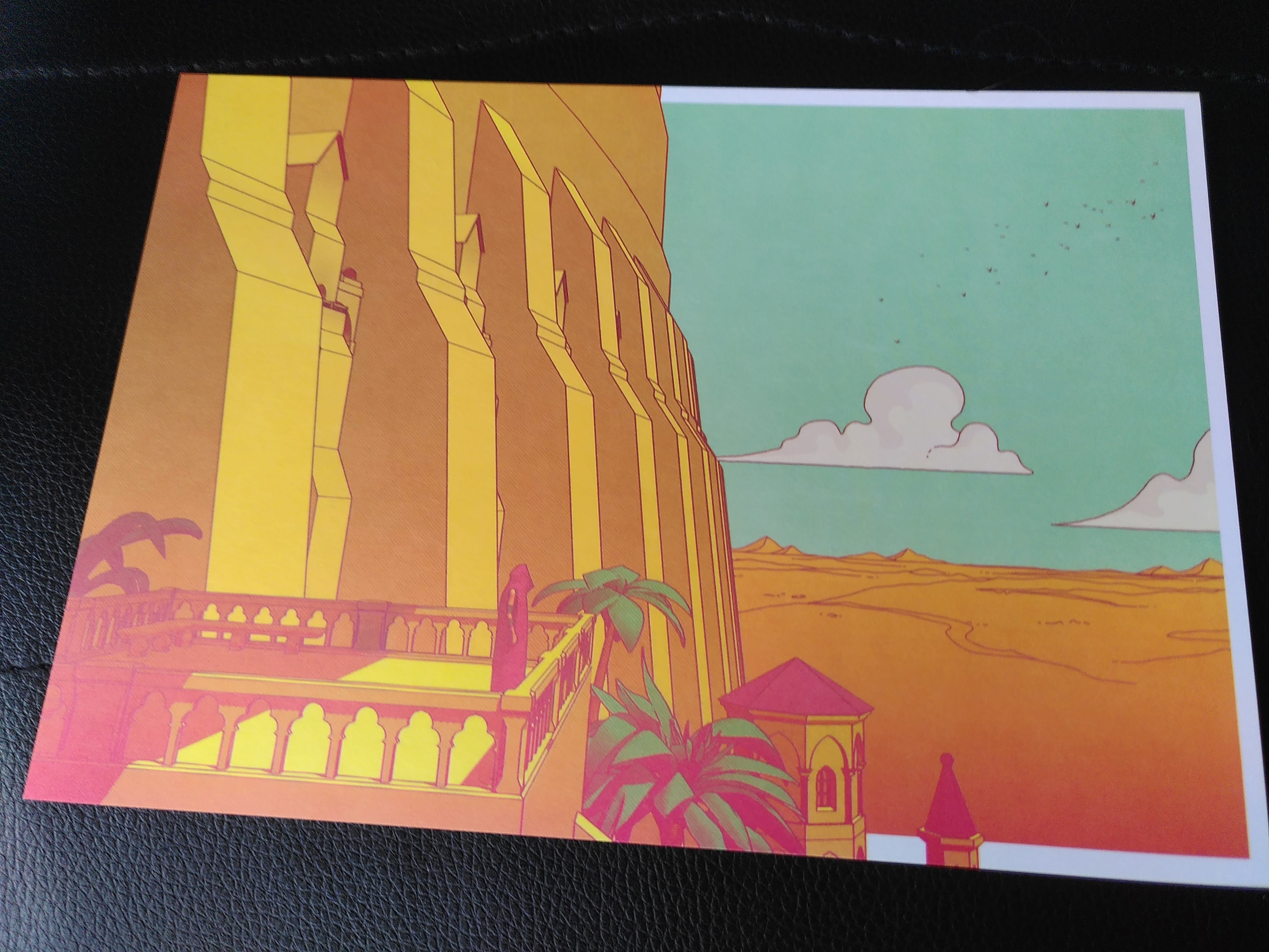 Photo d'un art print représentant un screenshot du jeu. Un décor en 3D avec un nombre limité de couleurs et nuances. On y voit notre protagoniste, de forme humaine, sous une toge brune, debout sur un balcon d'un immense bâtiment jaune se dressant au milieu d'un désert de sable sous un ciel bleu très clair.