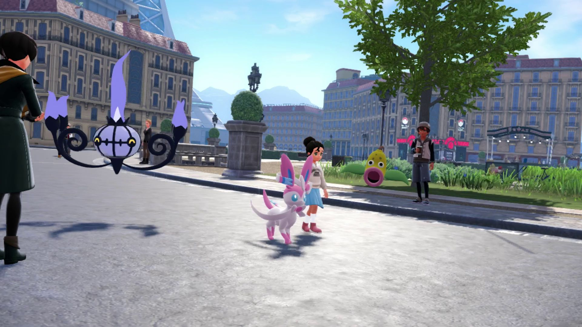 Screenshot du jeu montrant le personnage marcher dans la rue avec Nymphali (un Pokémon rose en forme de chien avec des rubans et des yeux bleus). On voit aussi un Lugulabre (Pokémon en forme de lustre avec des flammes violettes). On voit des ombres au sol dont on devine l'aspect pixelisé.