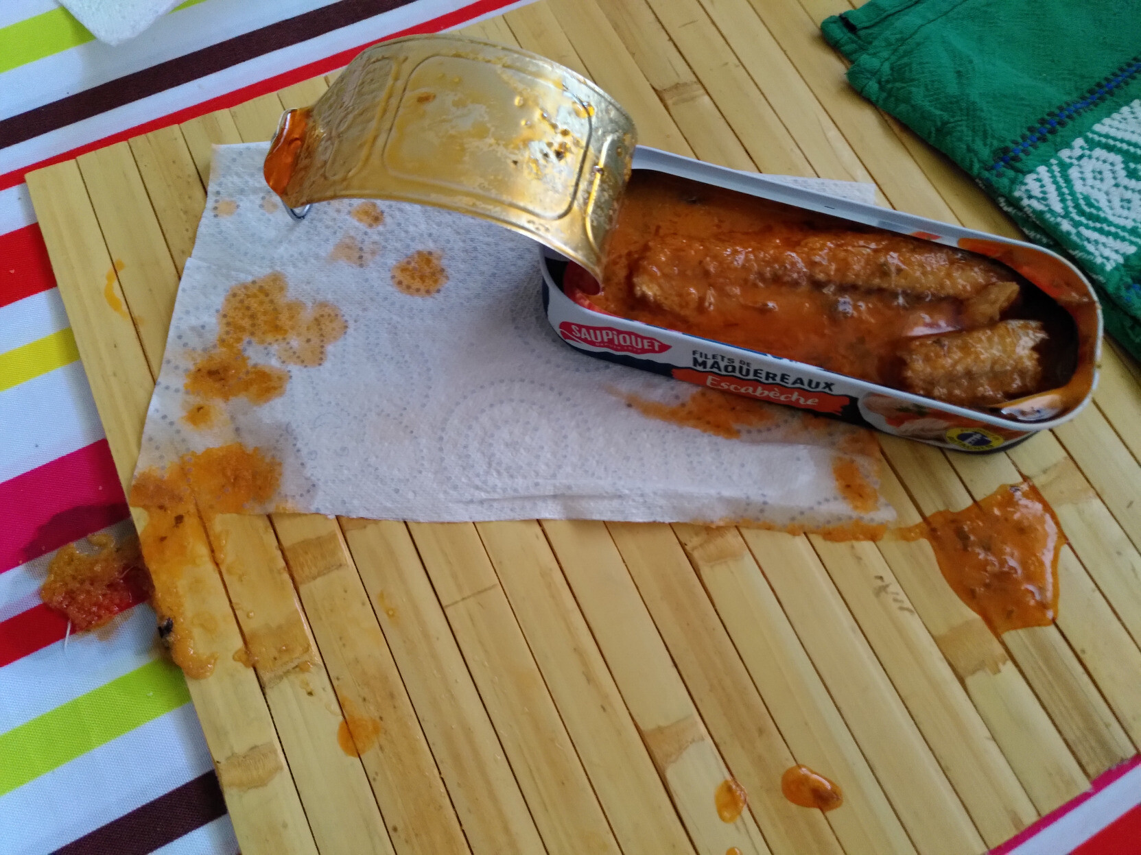 Une boite de maquereaux à l'escabèche ouverte, avec de la sauce ayant débordé à trois endroits différents autour de la boite de sauce.