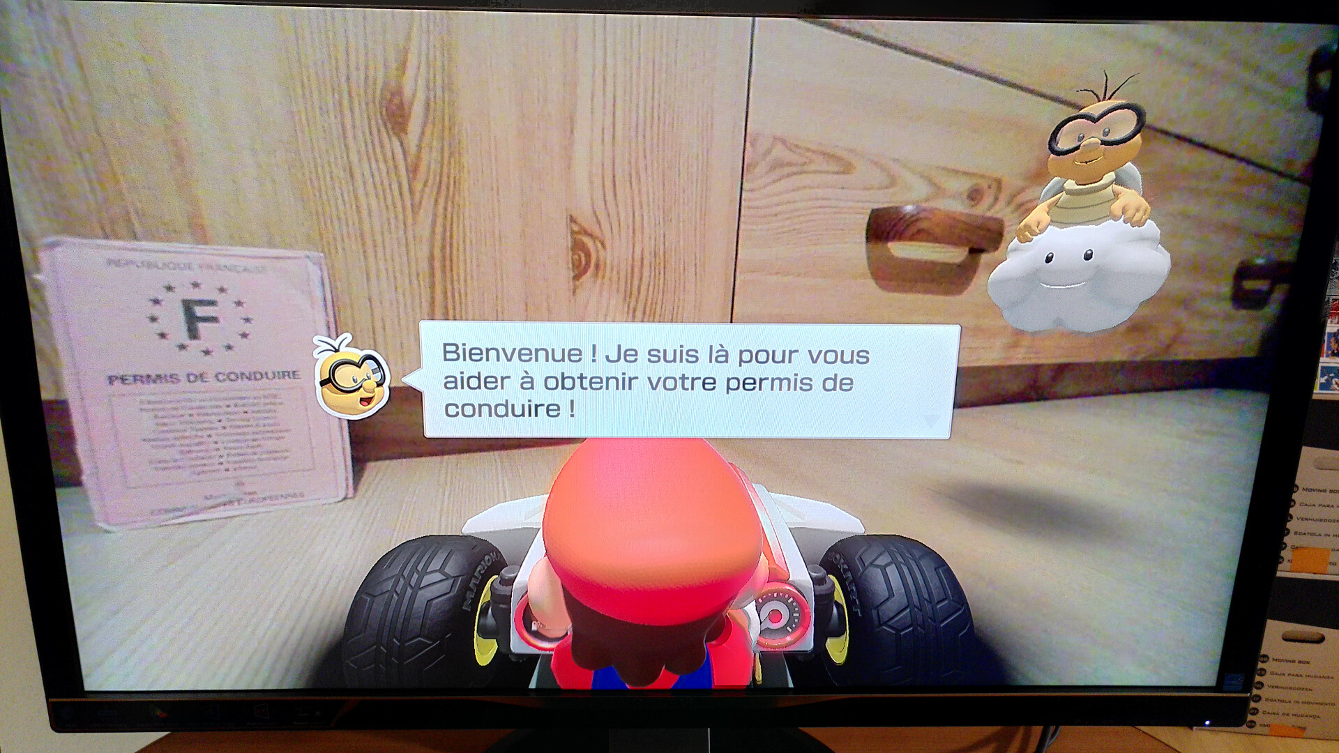 Screen du jeu Mario Kart Live : Home Circuit, avec Lakitu déclarant "Bienvenue ! Je suis là pour vous aider à obtenir votre permis de conduire !", j'ai mis mon vrai permis de conduire papier dans le champ de l'image pour faire une blague hilarante.